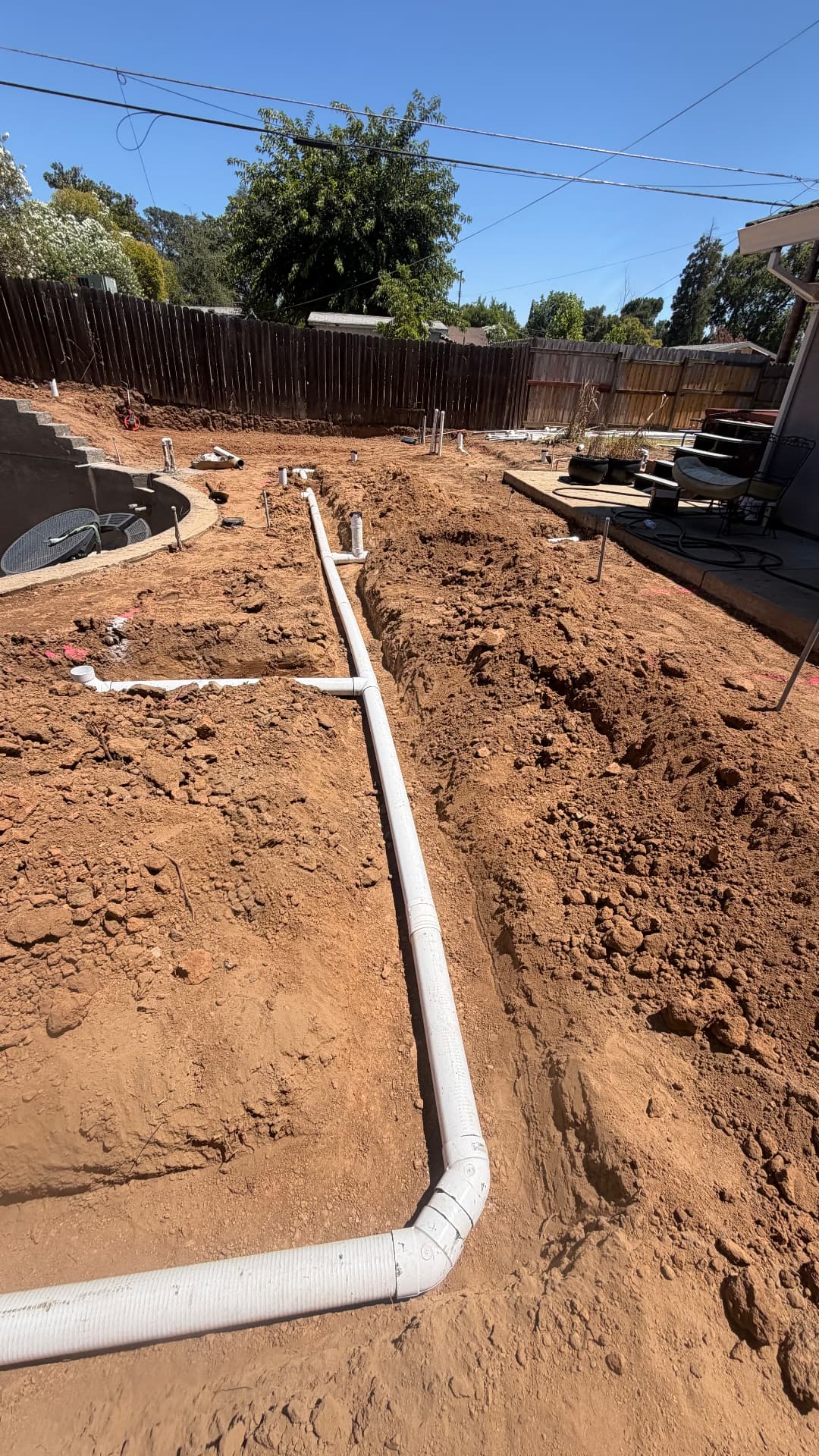 Underground drain and utility pipe trench run across a backyard job site
